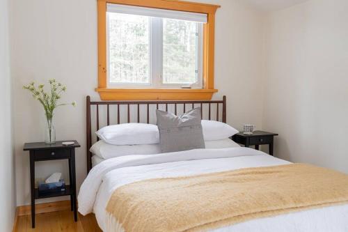 een slaapkamer met een bed met een raam en 2 tafels bij The Doma Lodge - Cozy Muskoka Cabin in the Woods in Huntsville