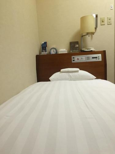 a bedroom with a white bed with a clock on the wall at Sky Heart Hotel Kawasaki in Kawasaki