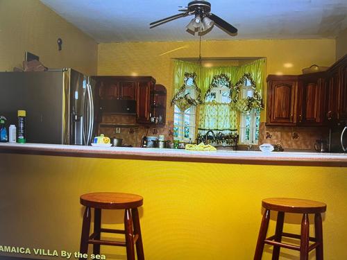 uma cozinha com um balcão amarelo e dois bancos de bar em Jamaica Villa By The Sea em St Mary