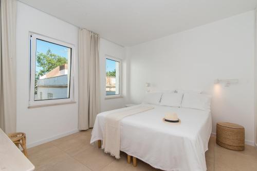 a white bedroom with a bed with a hat on it at Casa do Ser in Fuzeta