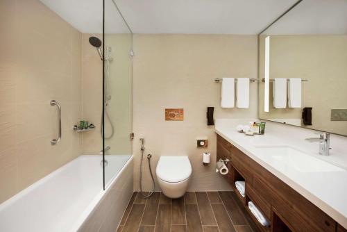 a bathroom with a toilet and a tub and a sink at Hilton Garden Inn Ras Al Khaimah in Ras al Khaimah