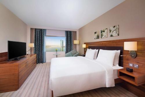 a bedroom with a large white bed and a flat screen tv at Hilton Garden Inn Ras Al Khaimah in Ras al Khaimah