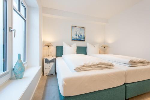 a white bedroom with two beds and a window at Haus Dünenweg Whg 2 in Hörnum