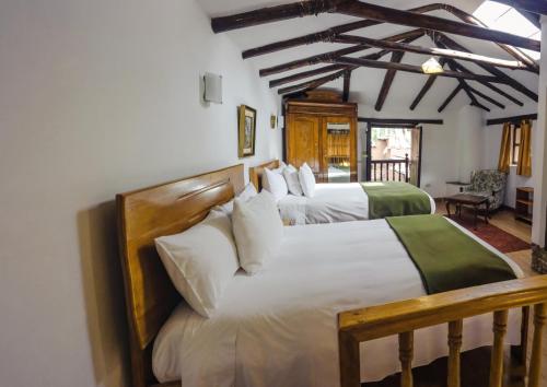 two beds in a room with white sheets at Lizzy Wasi Urubamba in Urubamba