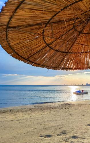 a beach with a straw umbrella and a boat in the water at CALM Blue Sea in Durrës