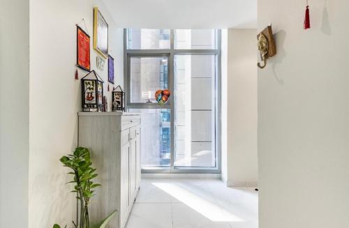 a white hallway with a window and a plant at Bright & Cozy, Near Metro & Downtown, Pool, Gym in Dubai