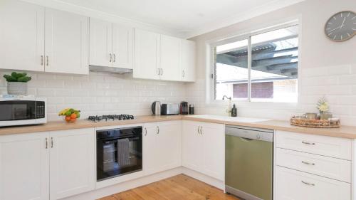 a kitchen with white cabinets and a clock on the wall at Bluebird Cottage in Bowral