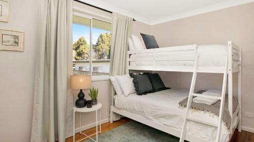 ein Schlafzimmer mit einem weißen Etagenbett und einem Fenster in der Unterkunft Bluebird Cottage in Bowral