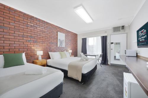 una camera d'albergo con due letti e un muro di mattoni di City Heart Motel Warrnambool a Warrnambool