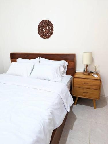 einem Bett mit weißer Bettwäsche und einem Nachttisch mit einer Lampe in der Unterkunft Tropical oasis private home in Krambitan