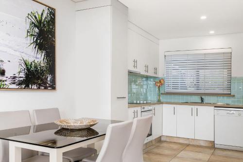 a kitchen with white cabinets and a table and chairs at Beach Break in East Ballina