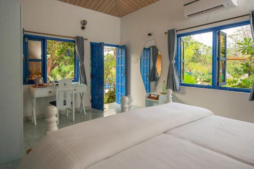 a bedroom with a white bed and a desk and windows at One At Goa in Canacona