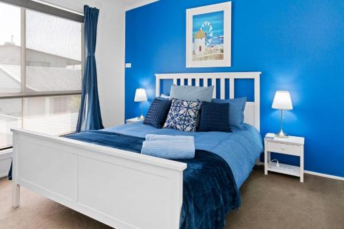 SANTORINI BEACH HOUSE SAFETY BEACH في سايفتي بيتش: غرفة نوم زرقاء مع سرير أبيض ونافذة
