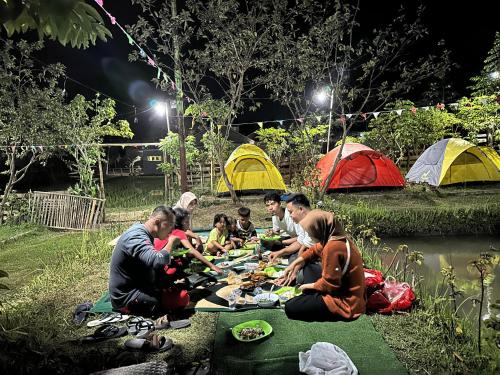 un gruppo di persone seduti intorno a un tavolo da picnic di fronte alle tende di Montong Raden camping ground a Midang