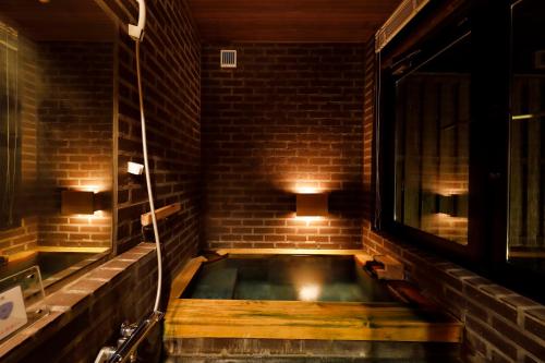 uma banheira num quarto com uma parede de tijolos em Ryokan Konomama em Minami Aso