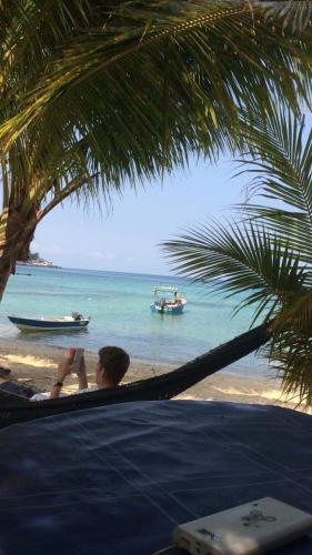 a man sitting in a hammock on a beach with boats in the water at Ella's Place Salang Tioman in Tioman Island