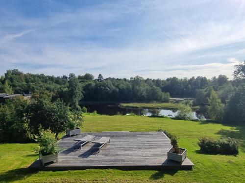 une terrasse en bois au milieu d'un champ avec un lac dans l'établissement Riverside villa, à Borlänge