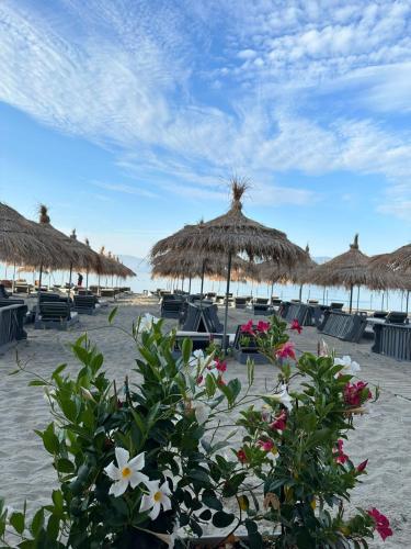 a beach with straw umbrellas and chairs and flowers at Villa Arli&Eris in Vlorë