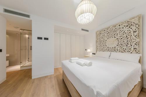 a white bedroom with a large bed and a chandelier at Apartamento Sevilla Centro in Seville