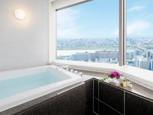 a bathroom with a bath tub and a large window at Hotel Hankyu International in Osaka