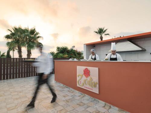 a man walks past a counter at a restaurant with chefs at Leonardo Laura Beach & Splash Resort in Paphos City