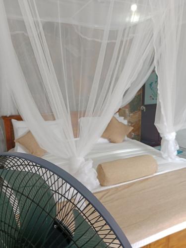 a bed with white curtains and a fan at Ella glory inn in Ella