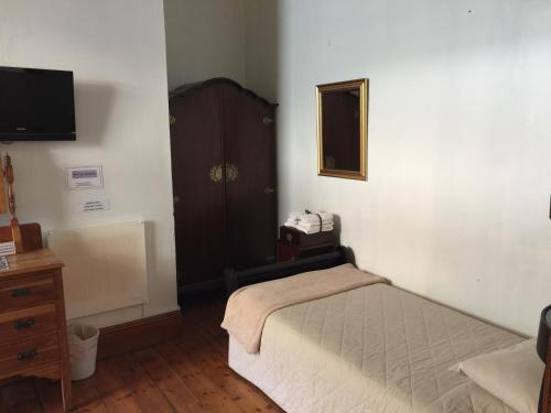 a bedroom with a bed and a dresser and a television at Central Hotel Guest House in Simonʼs Town