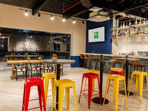 a restaurant with tables and yellow and red stools at Ibis Styles El Malecon Guayaquil in Guayaquil