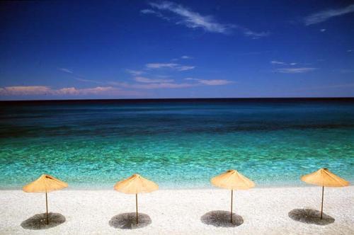 a group of umbrellas on a beach with the ocean at Mountain's Secret in Mouresi