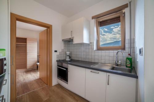 eine Küche mit weißen Schränken, einem Waschbecken und einem Fenster in der Unterkunft Gartenheim App Maria in Schenna