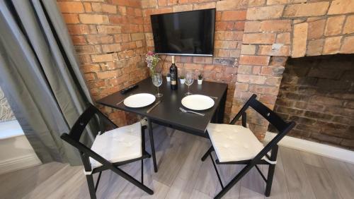einen schwarzen Tisch mit 2 Stühlen und einen TV an einer Backsteinwand in der Unterkunft Sunnyside Studio Apartment in Llandrindod Wells