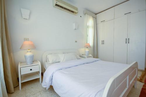 a white bedroom with a white bed and two lamps at Beach house First Row sea view at Santa Monica next to Almaza Bay in Marsa Matruh