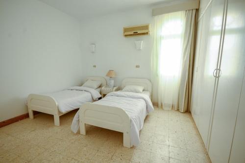 two beds in a white room with a window at Beach house First Row sea view at Santa Monica next to Almaza Bay in Marsa Matruh