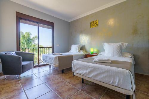 a bedroom with two beds and a chair and a window at La Huerta Del Sur in Alhaurín el Grande