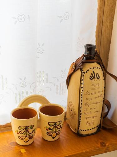 a couple of cups on a window sill next to a bottle at Lankás Vendégház - Hollókő in Hollókő