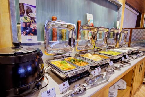 a buffet line with trays of food on a counter at Cozzet Victoria Hotel in Bhubaneshwar