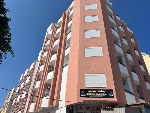 Un edificio alto, rosso e bianco, con un cartello sopra. di Residence ElFaracha a Sousse