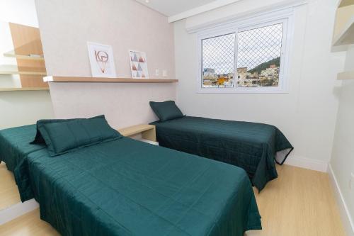 1 dormitorio con 2 camas verdes y ventana en Boulevard 221D - Excelente apartamento em condomínio de luxo no centro de Bombinhas - Piscina - Jacuzzi - Academia - Portaria 24h, en Bombinhas