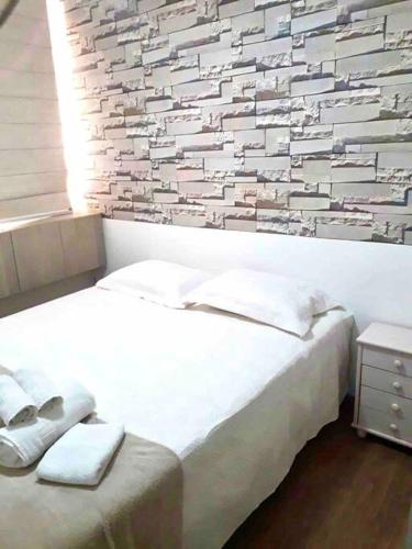 マリンガにあるMelhor custo benefício: elegância e conforto.の白いベッドとレンガの壁が備わるベッドルーム1室が備わります。