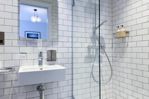 La salle de bains est pourvue de carrelage blanc, d'un lavabo et d'une douche. dans l'établissement THE KNIGHT OF NOTTINGHILL, à Londres