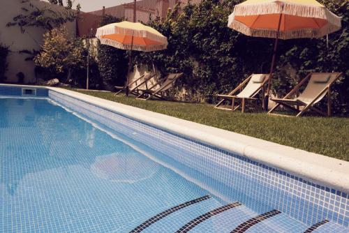 a swimming pool with two umbrellas and two lawn chairs and sidx sidx sidx at Hotel Palou 1874 in Sant Pere de Ribes