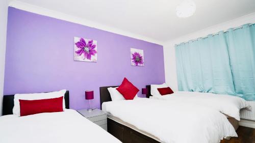 2 camas en una habitación con paredes moradas y almohadas rojas en E2M Stays Beautiful 6Bed Spacious House, en Cranford
