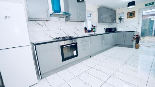 E2M Stays Beautiful 6Bed Spacious House في Cranford: مطبخ مع الأجهزة البيضاء وأرضية بلاط بيضاء