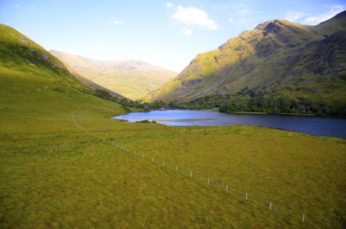 a field with a lake and a fence next to a mountain at Delphi Lodge in Leenaun
