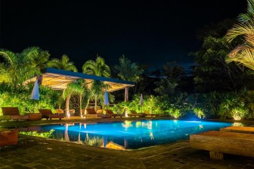 a pool at night with palm trees and a pavilion at El Rio Hotel in Doradal
