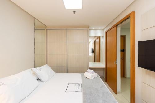 um quarto com uma cama branca e uma televisão em Conforto e Praticidade no Alto da Glória ESP2906 em Goiânia