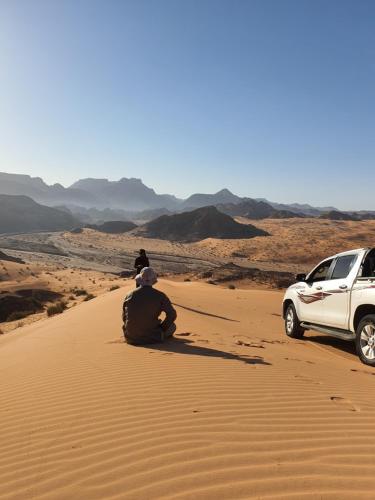 a man sitting in the desert next to a white truck at Bedouin Family Camp in Wadi Rum