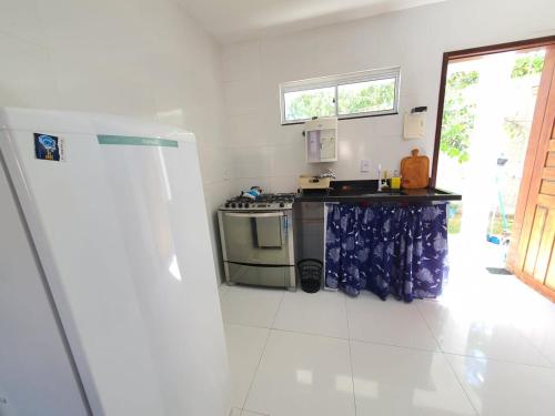 a white kitchen with a stove and a refrigerator at CASA NA RUA DO PIRUÍ EM AREMBEPE com ar in Arembepe