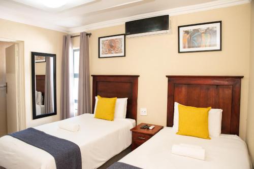 2 Betten in einem Hotelzimmer mit gelben Kissen in der Unterkunft M n M Guesthouse Polokwane Central in Polokwane