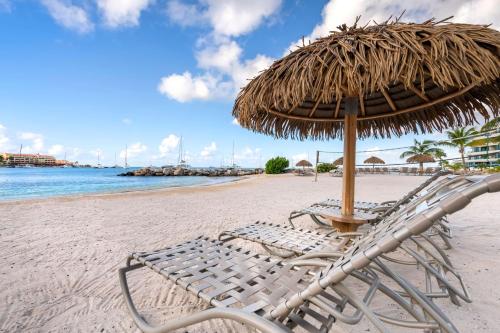 Hilton Vacation Club Royal Palm St Maarten في سيمبسون باي: مظلة القش والكراسي على الشاطئ